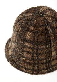 Cappello a secchiello in lana marrone con un motivo a quadretti, caratterizzato da una superficie texturizzata e morbida e una corona arrotondata. I bordi sono leggermente sfilacciati.