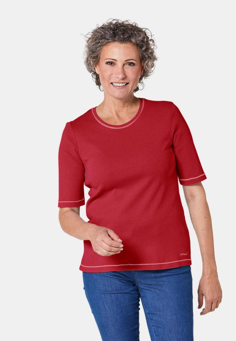 Rotes T-Shirt mit kurzen Ärmeln und rundem Ausschnitt sowie kontrastierendem gestepptem Saum. Aus strukturiertem Stoff gefertigt, kombiniert mit blauen Jeans.