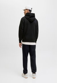 Schwarz hoodie, weiße T-Shirt darunter, dunkle Hose und helle Schuhe. Einfaches Design, gerippte Bündchen und Kängurutasche.
