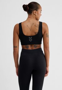 Zwarte sportbeha met brede banden, lage rug en witte chevron detail. Gecombineerd met zwarte leggings, met een gladde, elastische textuur.