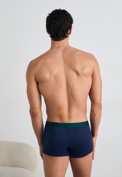 Marineblå boxershorts med grønn midjebånd. Tøyet ser glatt og elastisk ut, designet for komfort og passform. Synlige sømdetaljer.
