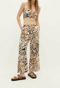 Dvoudílný outfit obsahující uzlový crop top a široké kalhoty s tygřím pruhem v odstínech béžové, černé a hnědé. Lehká tkanina.
