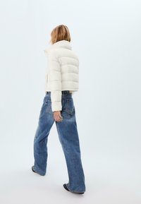 Puffjacka i off-white med horisontell sömnad, hög krage och dragkedja, kombinerad med blå oversized jeans.