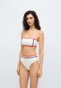 Επάνω μέρος λευκού στράπλες μπικίνι με κόκκινες λεπτομέρειες, συνδυασμένο με σλιπ ψηλόμεσο με κόκκινες και ναυτικές διακριτικές πινελιές, λεία υφή και μινιμαλιστικό σχέδιο.
