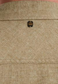 Beige látka s texturovaným tkaním, na horním zadním výstřihu s černou a zlatou visačkou "PME Legend".