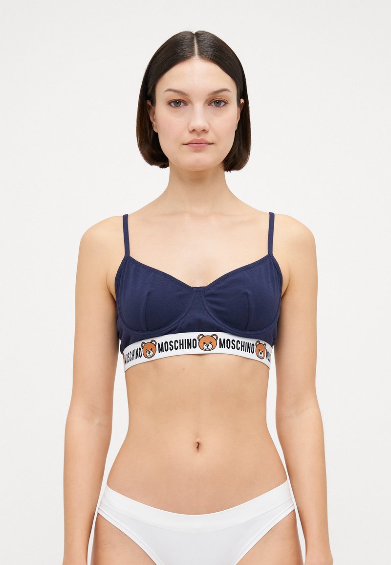 Navy cotton bralette with soft cups, adjustable straps, and a white waistband featuring a bear logo and "Moschino" text.