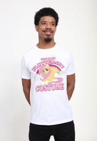 Bílý bavlněný tričko se barevným grafickým motivem kreslené poníka, s textem "TOHLE JE MŮJ KOSTÝM FLUTTERSHY" v růžové barvě.