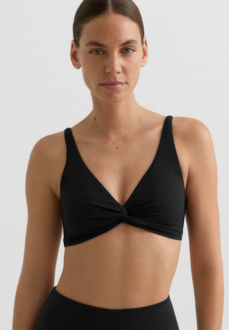 Bralette noir à torsade sur le devant avec larges bretelles, texture lisse et forme triangulaire. Design simple sans motifs ni accessoires supplémentaires.