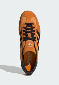 Tenisice s gornjim dijelom od narančaste velur kože, crnim akcentima i tri crne pruge. Sadrži teksturirani dizajn i crnu gumenu potplat.