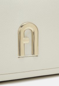 Vitt läderväska med detalj i guldig hårdvara och synlig sömnad. Texturen verkar slät och något texturerad.