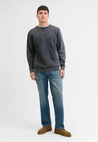Grijze pulloversweater met een ronde hals, gecombineerd met lichtblauwe versleten jeans. Bruine mocassinschoenen maken de look af.