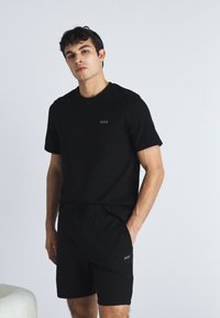 Tricou negru din bumbac, cu mânecă scurtă și un mic logo "BOSS" pe piept, asortat cu pantaloni scurți negri cu detaliu de logo.