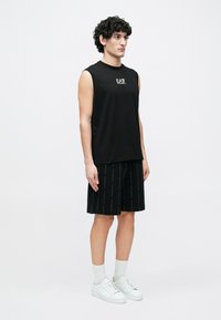 Mustad varrukateta t-särk logoga, mustade lühikeste pükstega, millel on õrn korduv tekstimuster, kantud koos valgete tossude ja sokkidega.