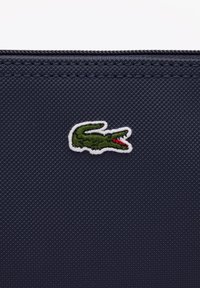 Trousse rectangulaire navy en tissu texturé. Présente un logo de crocodile vert brodé, souligné en blanc, sur le devant.