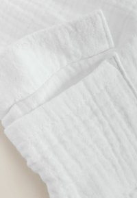 Deux tissus en coton blanc texturé pliés avec un motif gaufré sur un fond neutre.