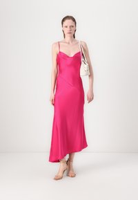 Fuchsia satin dress with a fluid silhouette, spaghetti straps, and a diagonal seam detail. Paired with a small white shoulder bag and nude heels.