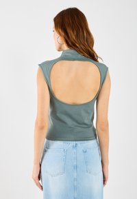 Grå ermeløs topp med høy krage og åpen ryggdesign, paret med en lyseblå denimskjørt med lommeapplikasjoner.