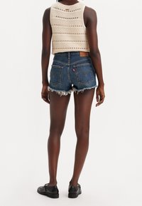 Řezané džínové šortky s třepenými lemy, zesílenými zadními kapsami a štítkem Levi's; doplněné krémovým pleteným krátkým topem s vodorovnými pruhy.