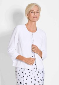 Witte geribde cardigan met een ronde hals en driekwartmouwen, voorzien van een knoopsluiting en een losse pasvorm over een gedrukt jurkje.