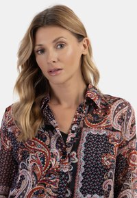 Camicia button-up con stampa paisley e pois in rosso, blu e nero. Tessuto leggero con colletto e maniche lunghe.