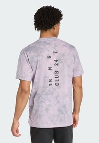 T-maica s kratkim rukavima u ljubičastom tie-dye uzorku s opuštenim krojem. Na stražnjoj strani se nalazi crni natpis "TRNG CLUB 24 7".