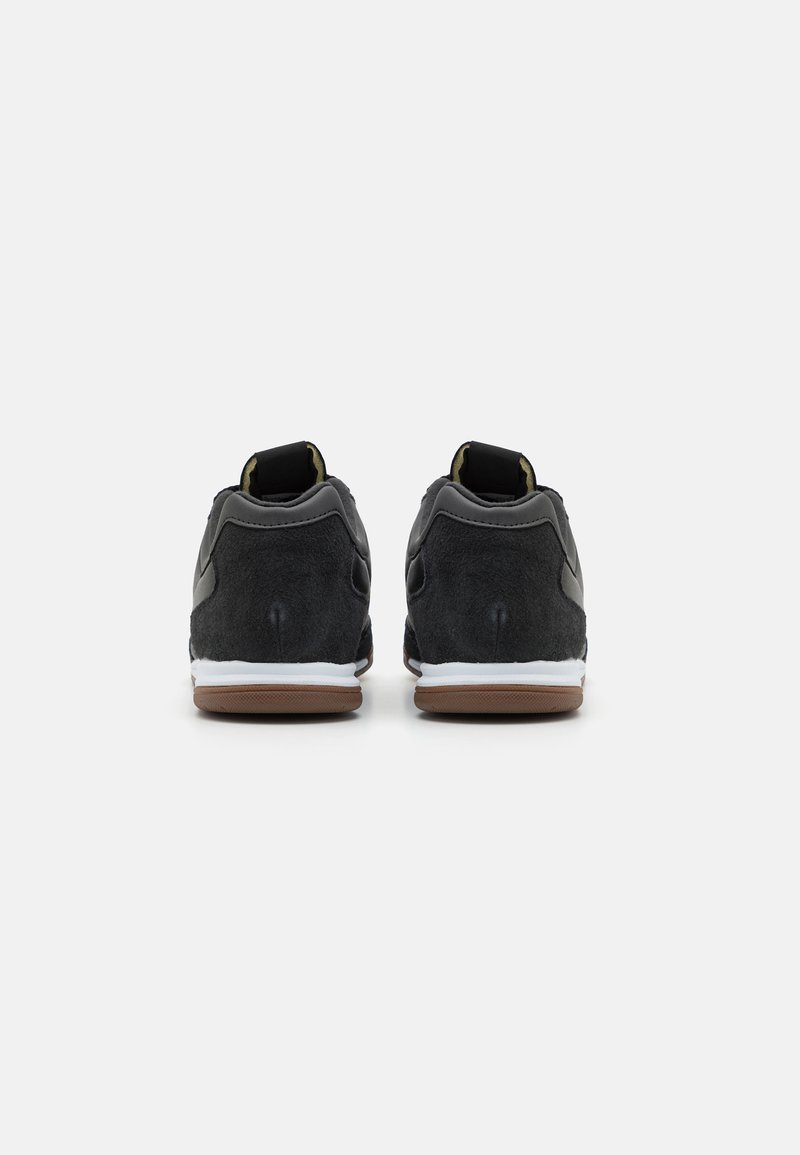 Scarpe sportive in suede nero con una suola intermedia bianca e una suola in gomma marrone. Presentano una tomaia testurizzata e una linguetta imbottita per il comfort.