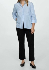 Chemise à rayures bleu clair avec des manches retroussées, associée à un pantalon noir à jambes droites. Des chaussures plates noires complètent le look.