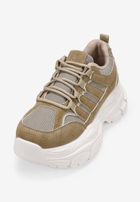 Zapatilla deportiva beige con parte superior de malla y cuero sintético, suela acolchada y un sistema de cordones detallado para un ajuste seguro.