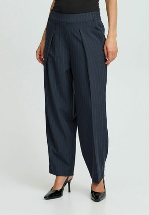 Marineblau gestreifte Hose mit lockerer Passform und elastischem Bund. Der Stoff hat eine glatte Textur, mit Falten, die für Detail sorgen. Kombiniert mit schwarzen High Heels.