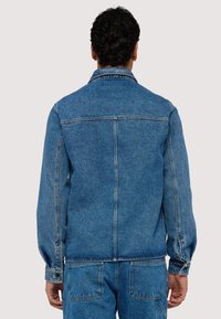 Jeansjacka i medelblått, har en klassisk krage, långa ärmar och elastiska manschetter. Bakstycket har två vertikala sömmar och inga synliga fickor.