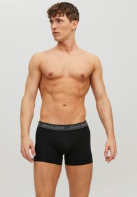 Schwarze Baumwollboxershorts mit einem elastischen Bund, der ein Logo trägt. Das Design ist figurnah mit einer glatten Textur und genähten Nähten.