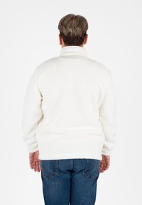 Witte fleece pull met hoge kraag, gestructureerd oppervlak en ingezakte schouders, gecombineerd met blauwe denim jeans.