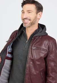 Maronfarbene Lederjacke mit abnehmbarer grauer Kapuze, Reißverschlusstaschen und grauem Innenfutter, teilweise offen präsentiert.