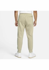 Lichtbeige joggers met een taps toelopende pijp, elastische tailleband en achterzak, gecombineerd met witte sneakers op een effen achtergrond.