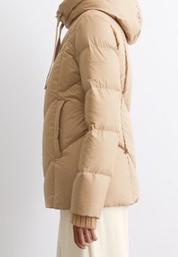 Beige Steppjacke mit figurbetontem Schnitt, Kapuze und Seitentaschen. Glattes, glänzendes Material mit horizontalen Steppnähten und gerippten Bündchen.