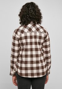 Camicia di flanella a quadri bianco e marrone con maniche lunghe e polsini con bottoni, caratterizzata da un orlo curvo e dettaglio sulla spalla.