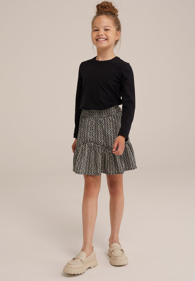 Černá košile s dlouhým rukávem, vzorovaná sukňa s volánem v černo-bílém diamantovém designu, béžové platformové boty s tlustou podrážkou.