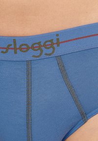 Blaue Sloggi-Unterhosen mit einem kontrastierenden grünen Logo am Bund. Verfügt über flache Nähte und eine glatte, dehnbare Stofftextur.