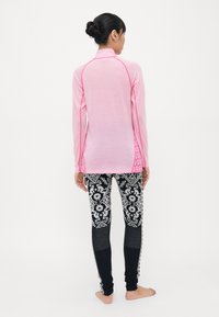 Langermet rosa treningsgenser med kontrasterende sømmer, parret med svarte leggings med mønster som har blomsterdesign og teksturerte detaljer.
