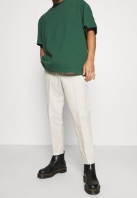 T-shirt vert en coton à manches courtes, associée à un pantalon beige clair effilé et des bottines en cuir noir à semelles épaisses.