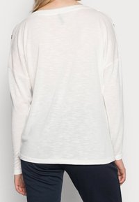Lekka, długosleeve'owa koszula w kolorze off-white z teksturowanym wykończeniem. Ma luźny krój oraz boczne wcięcia u dołu, co zapewnia swobodę ruchów.