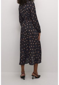 Svart långärmad klänning med cinchad midja och genomskinligt tyg, prydd med stora beigea prickar och midi-längd, i kombination med svarta klackar.