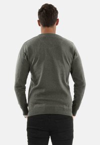 Grauer Strickpullover mit langen Ärmeln und Rundhalsausschnitt. Besitzt eine strukturierte Oberfläche sowie gerippte Bündchen und einen gerippten Saum. Schwarze Jeans sind darunter sichtbar.