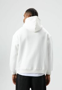 Witte hoodie van zachte stof, met een losse pasvorm en geribbelde boorden. Zichtbare stiksels en een gladde textuur aan de achterkant.