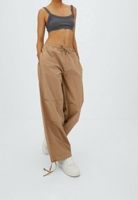 Bruine, losse cargo pants met een trekkoord in de taille, twee zijzakken en taps toelopende boorden. Gekoeld met een aansluitend grijs crop-top en witte sneakers.