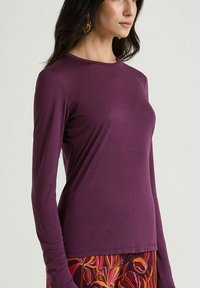 Maglia a maniche lunghe viola in tessuto morbido, con scollo rotondo e vestibilità comoda, abbinata a pantaloni con fantasia floreale.