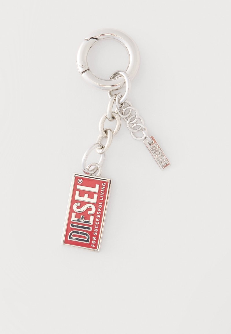 Porte-clés en métal argenté avec étiquette rectangulaire Diesel rouge et blanche et un petit charme Diesel attaché par des maillons de chaîne.