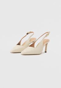 Kremfargede slingback-hæler med spiss tå, glatt patentfinish, tynn hæl, og justerbar stropp med gullfargede detaljer.