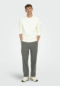 White crew-neck sweatshirt with ribbed cuffs, paired with gray pinstriped trousers and chunky white sneakers. Simple, casual design.