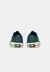 Tyrkysové semišové slip-on tenisky s nízkym profilom, bielou gumovou podrážkou a čiernym brandingom Converse All Star na päte.